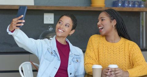 African american friends taking selfie laughing at coffee shop table with to-go cups
