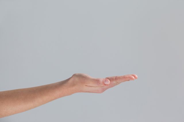 This image shows a close-up of a woman's cupped hand against a grey background. The open palm gesture can symbolize offering, support, or asking. It is ideal for use in advertisements, presentations, or websites that focus on themes of help, support, or minimalistic design.