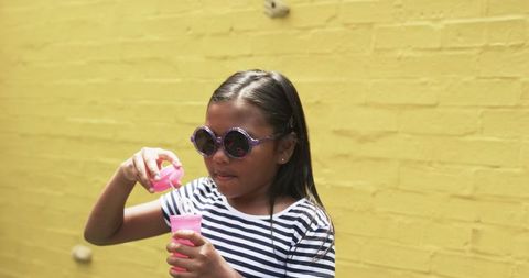 Stylish Young Girl Blowing Bubbles Against Yellow Wall
