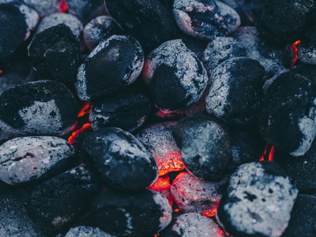 Evocative close-up shows glowing charcoal embers under a layer of ash, indicating high heat. Ideal for illustrating summer barbecue activities, outdoor cooking scenes, grill techniques, or promoting camping equipment and accessories. Perfect for food bloggers, barbecue enthusiasts, and outdoor lifestyle presentations.