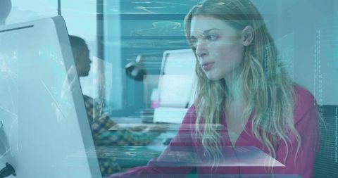 Blonde woman working at computer with holographic HUD overlay in modern open-plan office