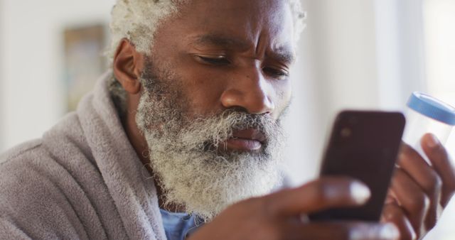 Senior man intensely focuses on smartphone while reading instructions for medicine bottle. Suitable for use in healthcare, senior living, and wellness articles, highlighting issues like medication management for older adults, and the use of technology in senior healthcare.