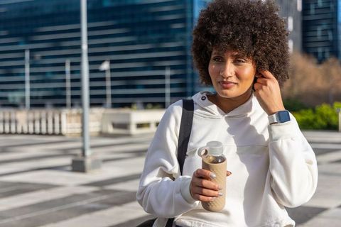 African american woman standing in urban plaza holding reusable bottle and backpack