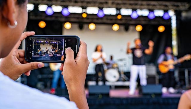 Female fan recording live band on smartphone at vibrant outdoor music stage under colorful lights