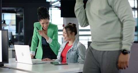 Indian coworker pointing at laptop while collaborating with colleague in modern office