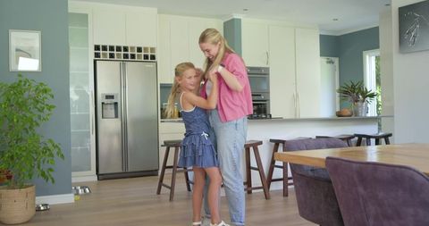 Mother and daughter dancing, laughing and hugging in bright modern open-plan kitchen