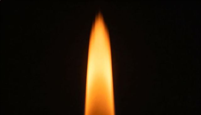 Burning amber flame rising against deep black background for warmth and contrast