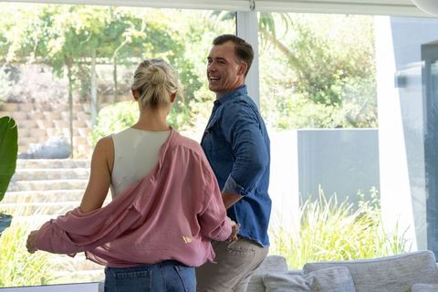Couple standing by sliding glass door smiling and enjoying sunny modern living room view