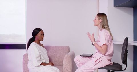 Nurse consulting with patient in clinic wearing pink scrubs using tablet for care planning