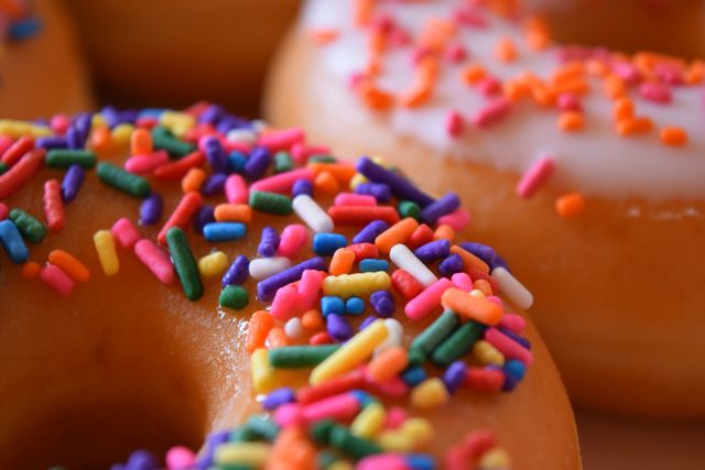 This image captures a detailed view of donuts covered with vibrant, colorful sprinkles and icing. Perfect for use in marketing materials for bakeries, dessert shops, or social media posts showcasing sweet treats. Additionally, it can be used in blog posts about dessert recipes, indulgent food concepts, or colorful food inspirations.
