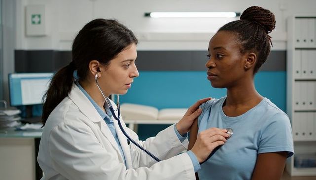 Doctor examining patient with stethoscope during clinical checkup in modern medical office