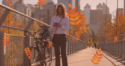 Hipster man on urban bridge using smartphone with autumn leaves