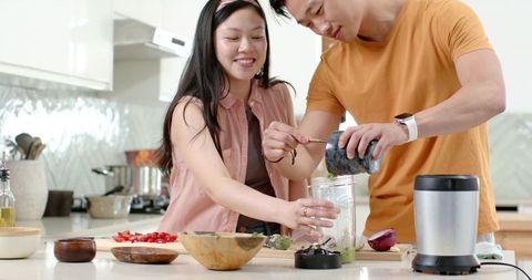 Asian couple preparing healthy green smoothie together in modern kitchen for wellness lifestyle