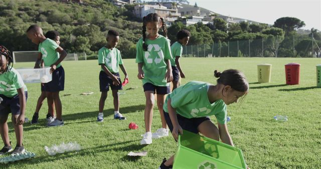 Group of children wearing green shirts with recycling symbols collecting litter in an open field with hills in the background. Engaging in an outdoor activity to promote environmental awareness and sustainability. Perfect for topics on environmental education, community engagement, teamwork, and promoting green initiatives among young people.