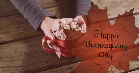 Cozy thanksgiving cocoa with marshmallows cradled in hands over rustic wooden table