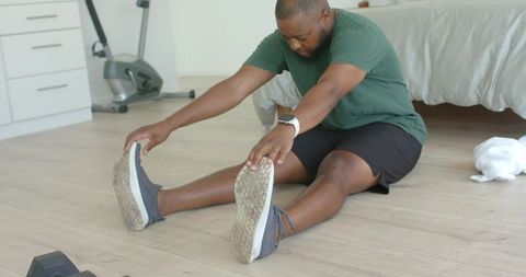 African american man stretching forward after workout in minimal bedroom home gym with dumbbells