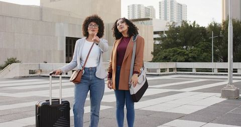 Female friends exploring urban plaza with luggage and smart casual blazers