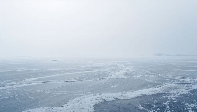 Frozen sea stretching to misty horizon with cracked ice, snowdrifts and minimal monochrome