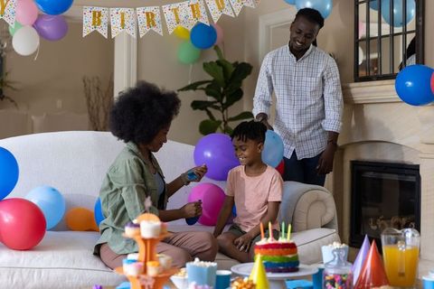 African american family celebrating birthday at home with rainbow cake and colorful balloons