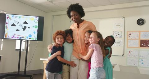 African American teacher hugging diverse elementary students in bright modern classroom