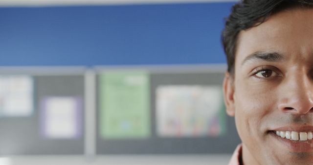 Young man smiling indoors with focus on part of his face. Background shows blurred wall decor. Perfect for promoting positivity, mental health, customer service or educational content.