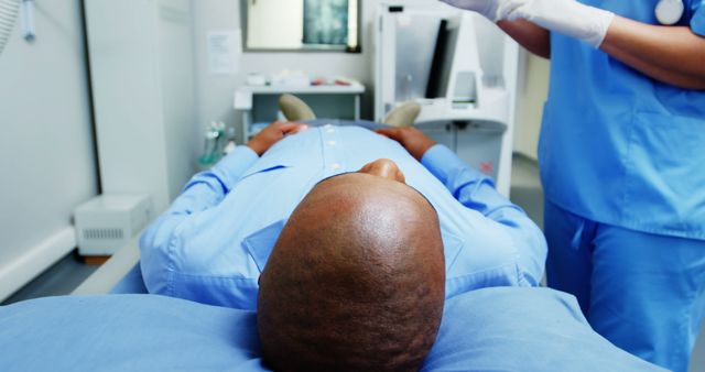 Patient lying down receiving medical examination by healthcare professional in modern hospital room. Ideal for topics related to patient care, healthcare services, medical treatment, clinical environments, and doctor-patient interactions.