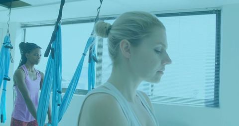 Women practicing aerial yoga in modern studio with blue hammocks