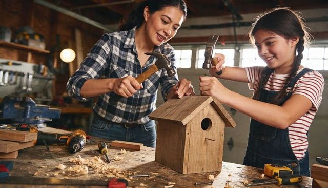 Mother and daughter building rustic birdhouse in garage workshop, hands-on diy bonding