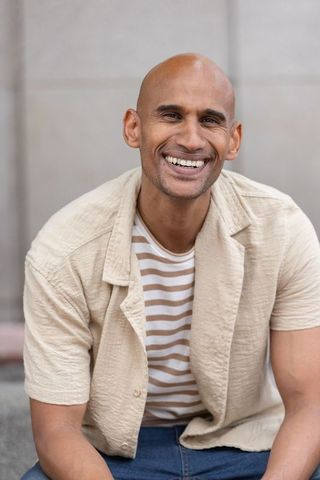 Confident african american man smiling and leaning forward in casual beige shirt and jeans