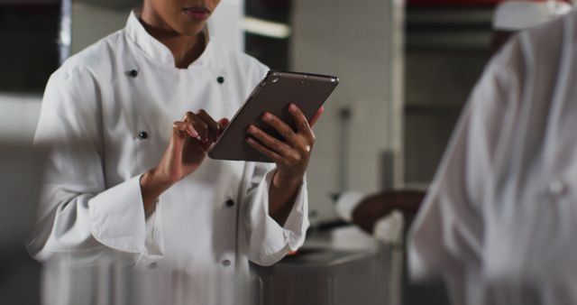 African american female chef using tablet in restaurant kitchen. Working in a busy restaurant kitchen.