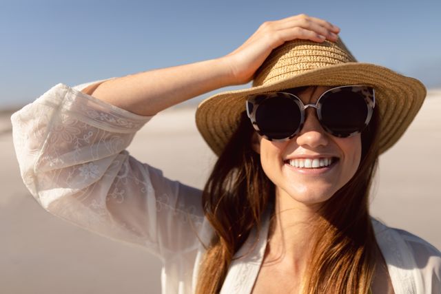 Beautiful woman in hat and sunglasses standing on beach in the sunshine