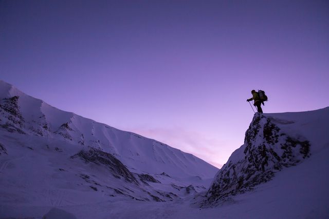 Hiker standing on a cliff in snowy mountains during sunrise. Ideal for themes related to adventure, winter sports, and outdoor activities. Useful for websites and brochures promoting hiking trips, nature explorations, and mountain climbing excursions.