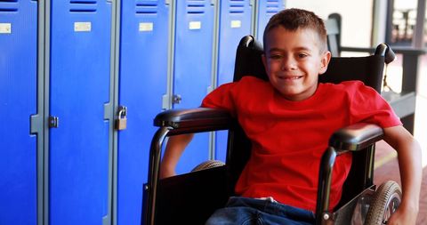 Smiling schoolboy in wheelchair by blue lockers