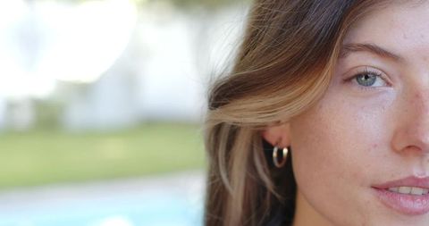 Sunlit backyard portrait of woman gazing by pool showing freckles and gold hoop earring