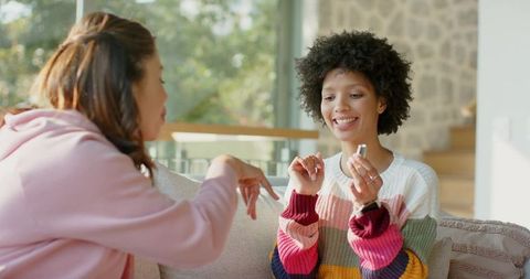 Friends sharing manicure moment on couch in sunlit living room