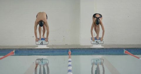 Synchronized swimmers preparing for race on starting blocks
