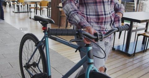 Urban cyclist standing with teal bicycle in cafe wearing plaid shirt and ripped jeans