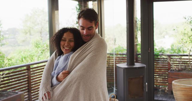 Smiling biracial couple wrapped in sheets embracing each other in the balcony at vacation home. couple honeymoon and vacation concept