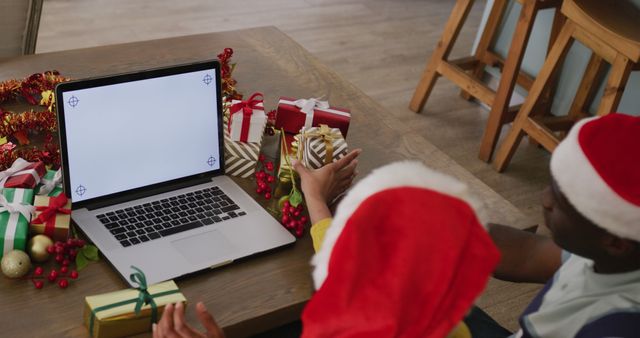 Image of diverse couple in santa hats making christmas laptop image call, with copy space on screen. Christmas, communication, tradition, celebration and inclusivity concept.