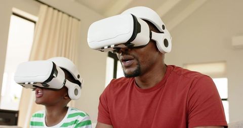 African American Father and Son Immersing in Virtual Reality Gaming Together on Couch