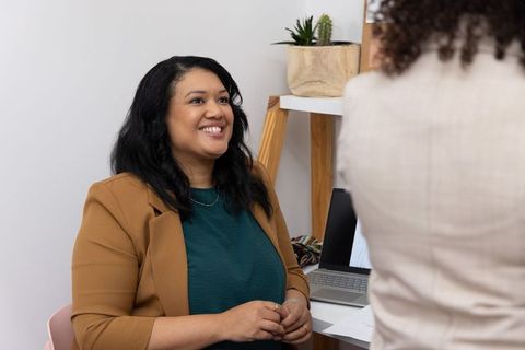 Smiling diverse female coworker consulting colleague at modern office workspace