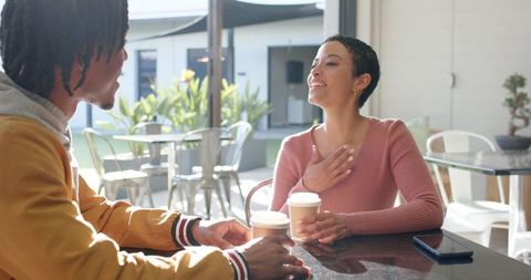 Diverse friends sharing coffee and laughing in sunlit modern cafe courtyard