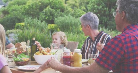 Multigenerational family sharing outdoor meal on wooden table in lush garden