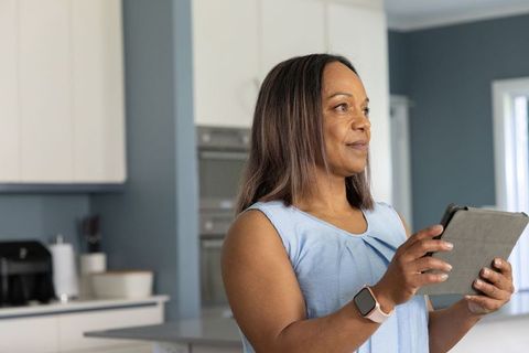 Mature woman using tablet and checking smartwatch in modern kitchen