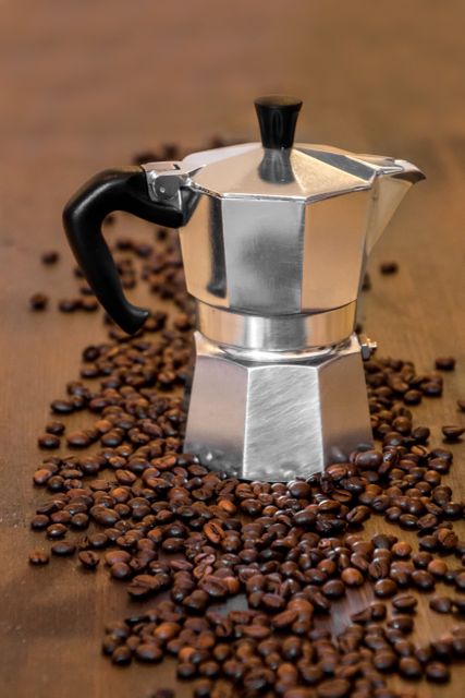 Stainless steel espresso maker placed among roasted coffee beans. This image captures the essence of a traditional coffee brewing method and can be used for kitchen appliance advertisements, coffee shop decor, food and drink promotions, or lifestyle blogs focused on coffee culture.
