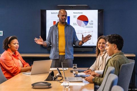 Diverse team collaborating in boardroom with presenter explaining revenue charts