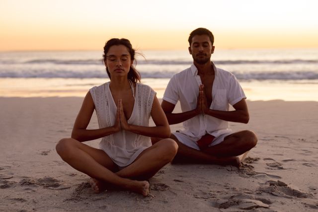 Couple performing yoga together on the beach during sunset