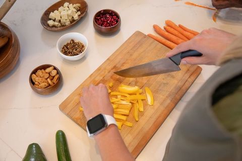 Hand slicing yellow pepper in kitchen with fresh ingredients