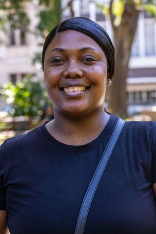 Confident woman smiling in urban park wearing black tee and crossbody bag, natural daylight headshot