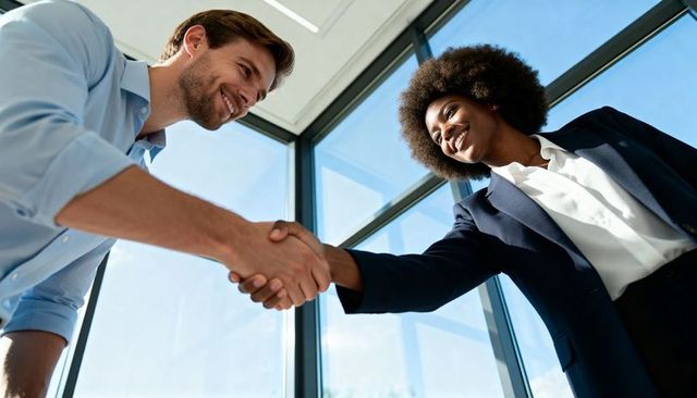 Smiling professionals shaking hands in glass office for successful business partnership
